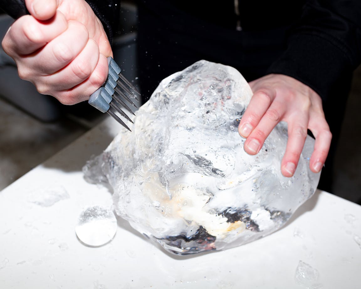 A person uses a tool to carve into a chunk of ice.